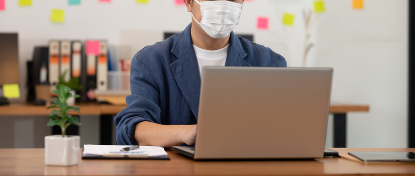 Banner Asian senior business man in casual wearing mask working with laptop in modern office or co-working space Due Covid-19 Flu Pandemic,Health care and Business Startup Concept