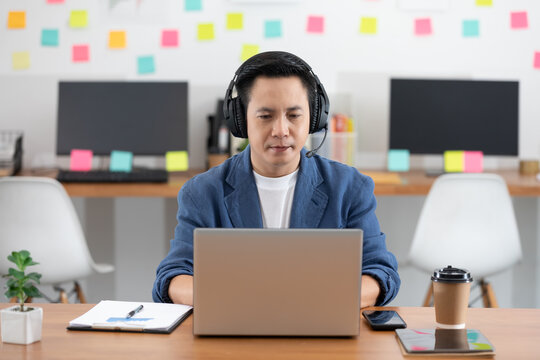 Asian Senior business man wearing earphone meeting with business team via video conference call at Home or Co-Working Space or Startup Office