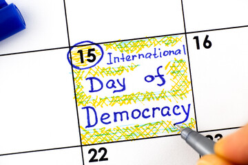 Woman fingers with pen writing reminder International Day of Democracy in calendar.