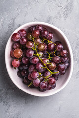 Fresh ripe grape berries in bowl on stone concrete background, top view
