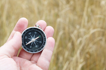 Old classic navigation compass in hand on natural background as symbol of tourism with compass,...