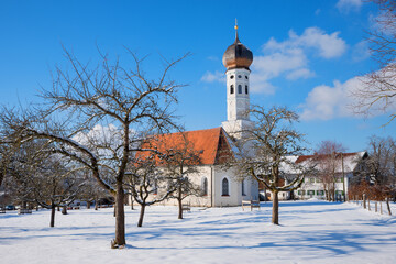 typical bavarian church in winter landscape, bare-leaved apple trees