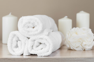 set of white terry towels on a background of candles and a washcloth concept of relaxation bathroom and spa accessories soft focus