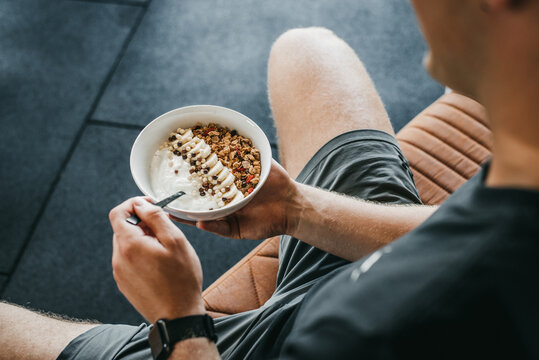 Man Eating healthy breakfast bowl on The Couch. Yogurt, granola, seeds, fresh and dry fruits and honey in blue white bowl. Clean eating, dieting, detox, vegetarian food concept