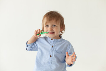 Boy 2 years old in a blue shirt on a white background brushing his teeth