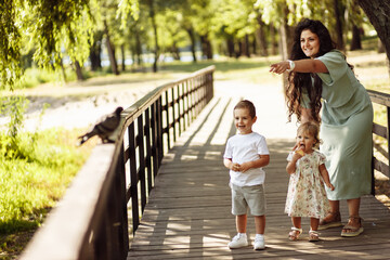 Caring mother with happy son and adorable daughter at the park, beautiful woman show a bird to the little kids, smiling, enjoy family moments, motherhood and childhood concept