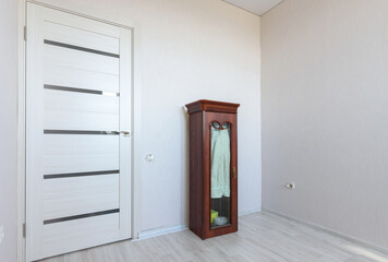 A fragment of a small bedroom in an apartment with poor furniture, a view of the front door and a locker