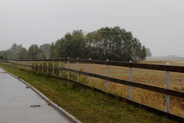 Fototapeta na wymiar Empty paddock area during rain. Gray rainy day at coutryside, pasture fence next to road.