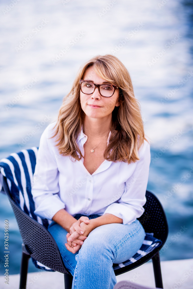 Wall mural Portrait of attractive mature woman sitting on chair by the sea