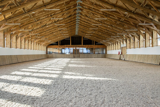 Empty spacious riding hall interior view. Sunlight through windows. Modern equestrian place.