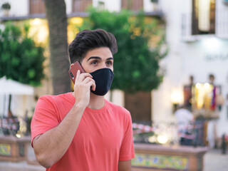 Hombre joven hablando y usando su teléfono móvil usando mascarilla respetando las normas de...