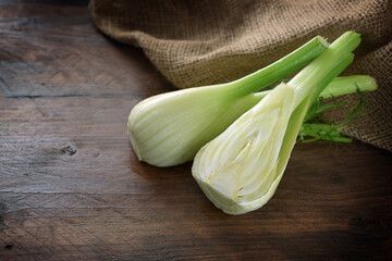 Halved raw fennel bulb on a dark rustic wooden table, healthy Mediterranean vegetable, copy space, selected focus, narrow depth of field
