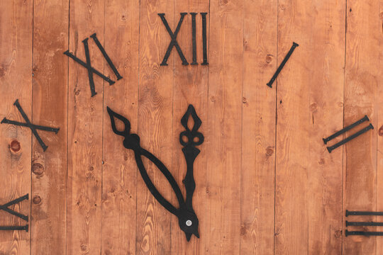 Layout clock. Dial with Roman numerals. Textured brown planks wood base. Black hands of the clock show the time - five minutes to twelve. New Year holiday concept.