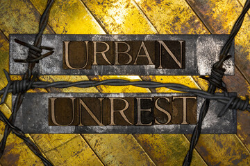Urban Unrest text formed by real authentic typeset letters with barbed wire on vintage textured grunge copper and gold background