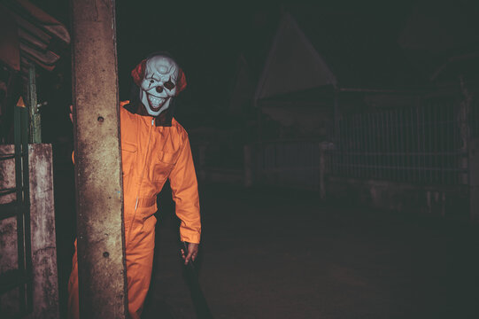 Asian handsome man wear clown mask with weapon at the night scene,Halloween festival concept,Horror scary photo of a killer in orange cloth
