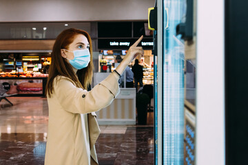 woman with a face mask uses the vending machine to buy a snack