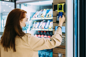 woman with a face mask uses her credit card to pay at the vending machine