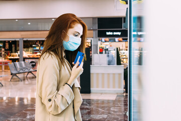 Fototapeta premium woman with a face mask uses her credit card to pay at the vending machine