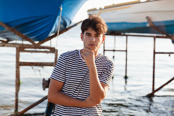 Portrait of a young man in striped t-shirt staying against the background of the boats on the sea. ...