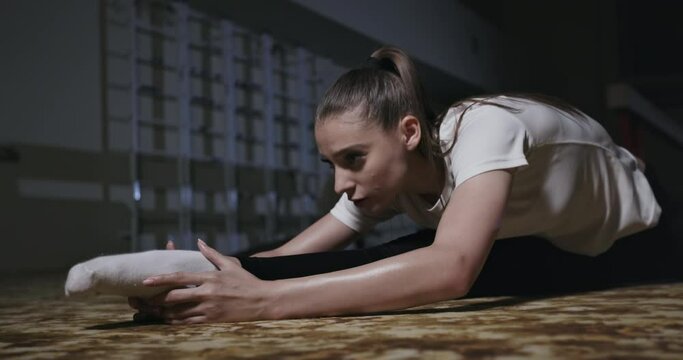 Determined sweaty ballerina training hard and performing forward bend while sitting on split and stretching legs in sports studio