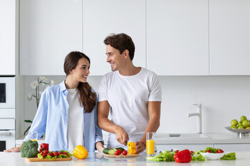 Obraz na płótnie Canvas Cute couple cooking in kitchen, man chopping vegetables.