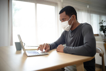 Portrait of handsome African American man with medical mask while working at desk at home during corona virus outbreak. Concept business people working at home,Remote,freelancer.COVID-19 epidemic.