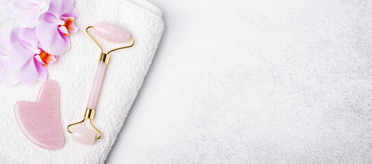 Horizontal banner with Rose Quartz jade roller, Gua Sha massager and orchid flower on stone background
