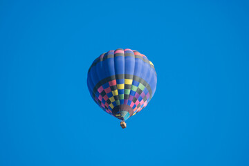 Blue patterned hot air balloon rises up overhead on a clear blue sky.  Fun adventure tourist activity allows for wonderful views from above.