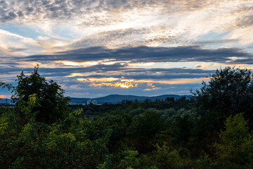 Beautiful orange sky with the sunset peaking through the clouds over Vienna Austria with a view of the city, green trees and mountains