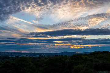 Obraz premium Striking orange sky with the sunset peaking through the clouds over Vienna Austria with a view of the city, green trees and mountains