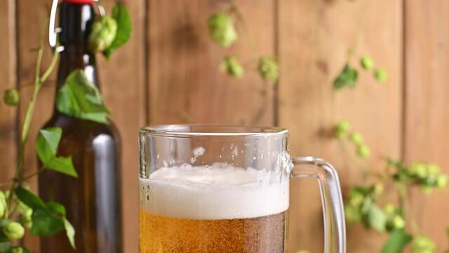 Beer. Cold Craft light Beer in a glass with water drops. Pint of Beer close up on a wooden background. Beer is pouring from the bottle. Border design. High quality 4k footage