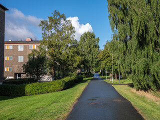 View of a walkway in a suburb to Gothenburg, Sweden. Large birch trees and tennant buildings are visible.