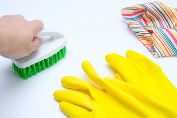 Yellow rubber gloves, microfiber wipe lying on white surface and a hand cleaning it with a brush, housecleaning and housework concept, house hygiene and sanitary protection