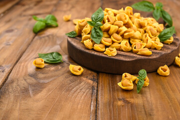 Fototapeta na wymiar Tortellini mignon on a wooden board with basil and parmesan. Specialties of the cuisine from Bologna and Emilia Romagna: Cappelletti, fresh egg pasta with meat and vegetables filling. Copy space