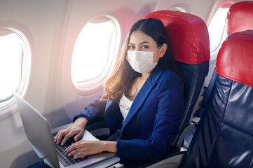 A young businesswoman wearing face mask is using laptop onboard, New normal travel after covid-19...