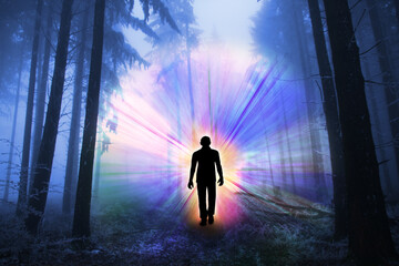 black silhouette of a man with luminous rays of energy in a dark forest on the road among the...