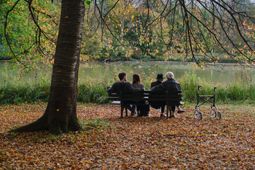 Senior couple man and woman and a young couple are resting on a bench in the autumn park.