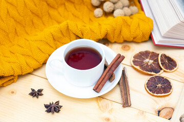 aromatic hot cinnamon tea covered with a warm scarf on a wooden autumn background.