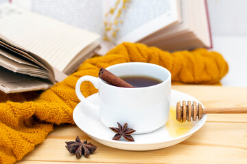 aromatic hot cinnamon tea covered with a warm scarf on a wooden autumn background. honey dipper with honey. comfortable reading a book