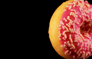Close-up view of pink glazed donut with sprinkles.