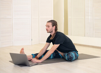 A young male yogi practices and teaches yoga online on a laptop in the Studio, performing and...