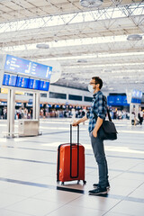 Airport European nerd man in glasses and plaid shirt with luggage tourist boarding plane taking a flight wearing face mask. Coronavirus flu virus travel 