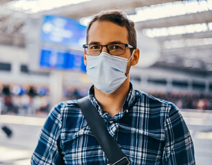 Airport European nerd man in glasses and plaid shirt with luggage tourist boarding plane taking a flight wearing face mask. Coronavirus flu virus travel 