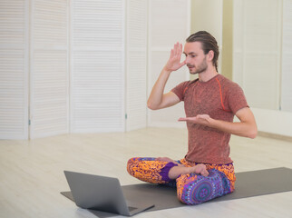A young male yogi practices and teaches yoga online on a laptop in the Studio, performing and...