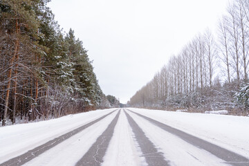 Obraz premium Patterns on the winter highway in the form of four straight lines. Snowy road on the background of snow-covered forest. Winter landscape.