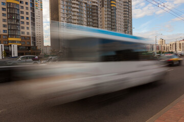 The movement of a blurred minibus along the avenue in the daytime.