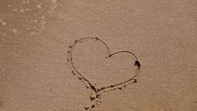 girl draws a heart on the beach. Sea water washes away the drawing on a sandy beach.