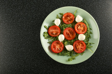 salad with mozzarella cheese, herbs and tomatoes top view on black table