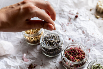 Hands take a pinch of spice from a glass jar. Dried flowers, lavender and rosemary