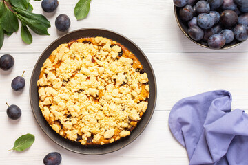 Delicious juicy plum cake in a round plate on a white wooden background, plum tree leaves with fruits